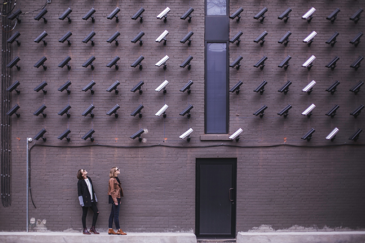 two women next to brick wall with CCTV surveillance cameras pointing at them