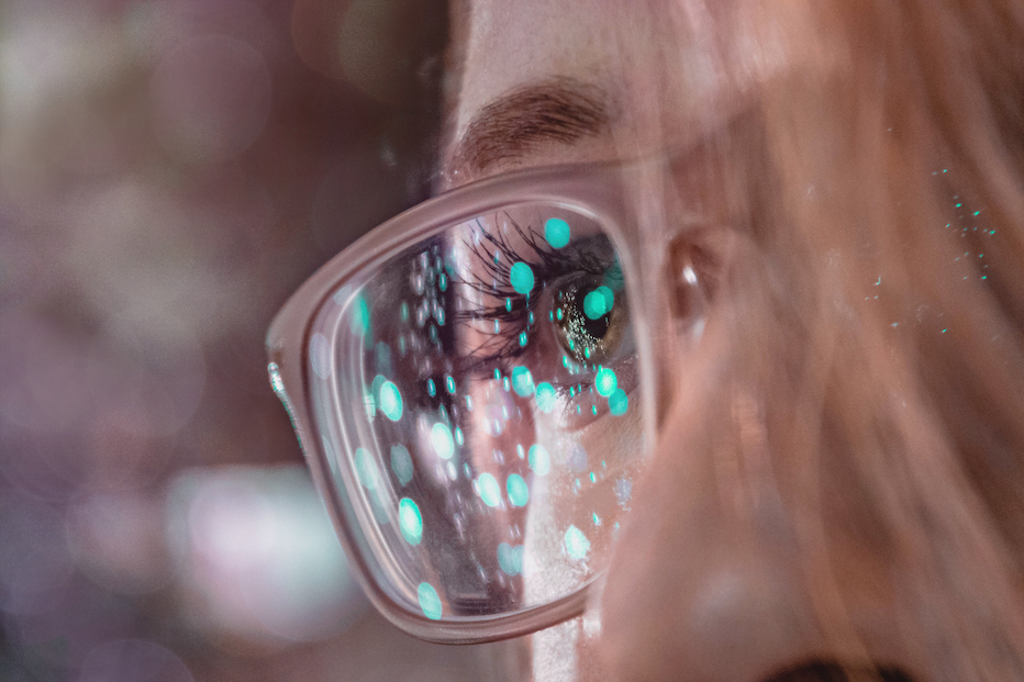 blue light array reflected in blonde girl's clear framed glasses looking privacy